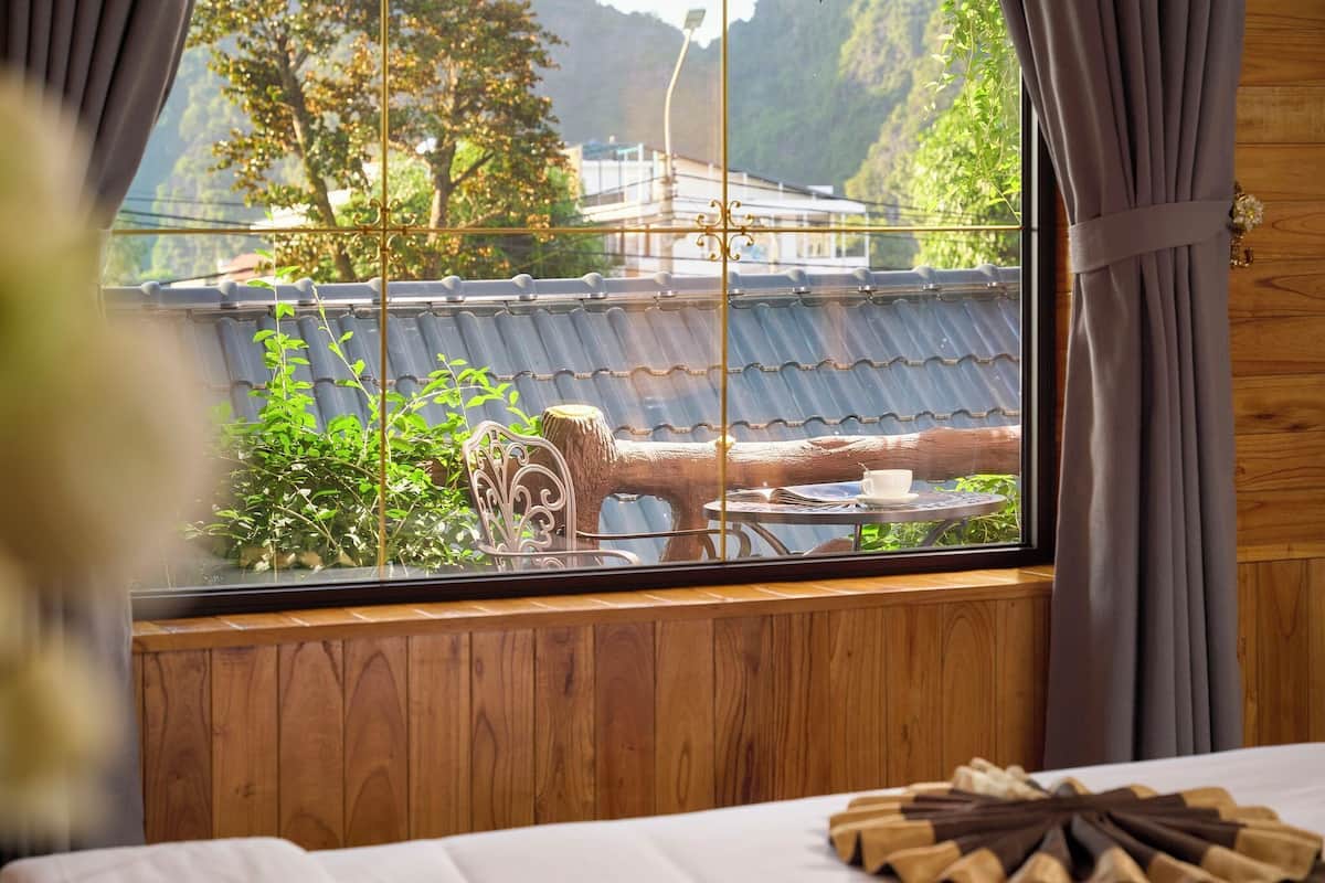 Une pièce au décor intérieur en bois, une fenêtre donnant sur un bâtiment traditionnel et sur de la verdure, ainsi qu’une petite table avec une tasse et une soucoupe.