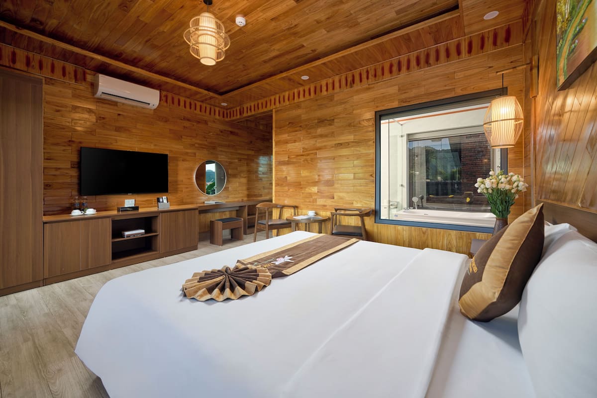 Une chambre d’hôtel avec un plafond en bois, un téléviseur à écran plat, un grand lit agrémenté d’un couvre-lit décoratif, une petite table et une fenêtre donnant sur un paysage agréable.