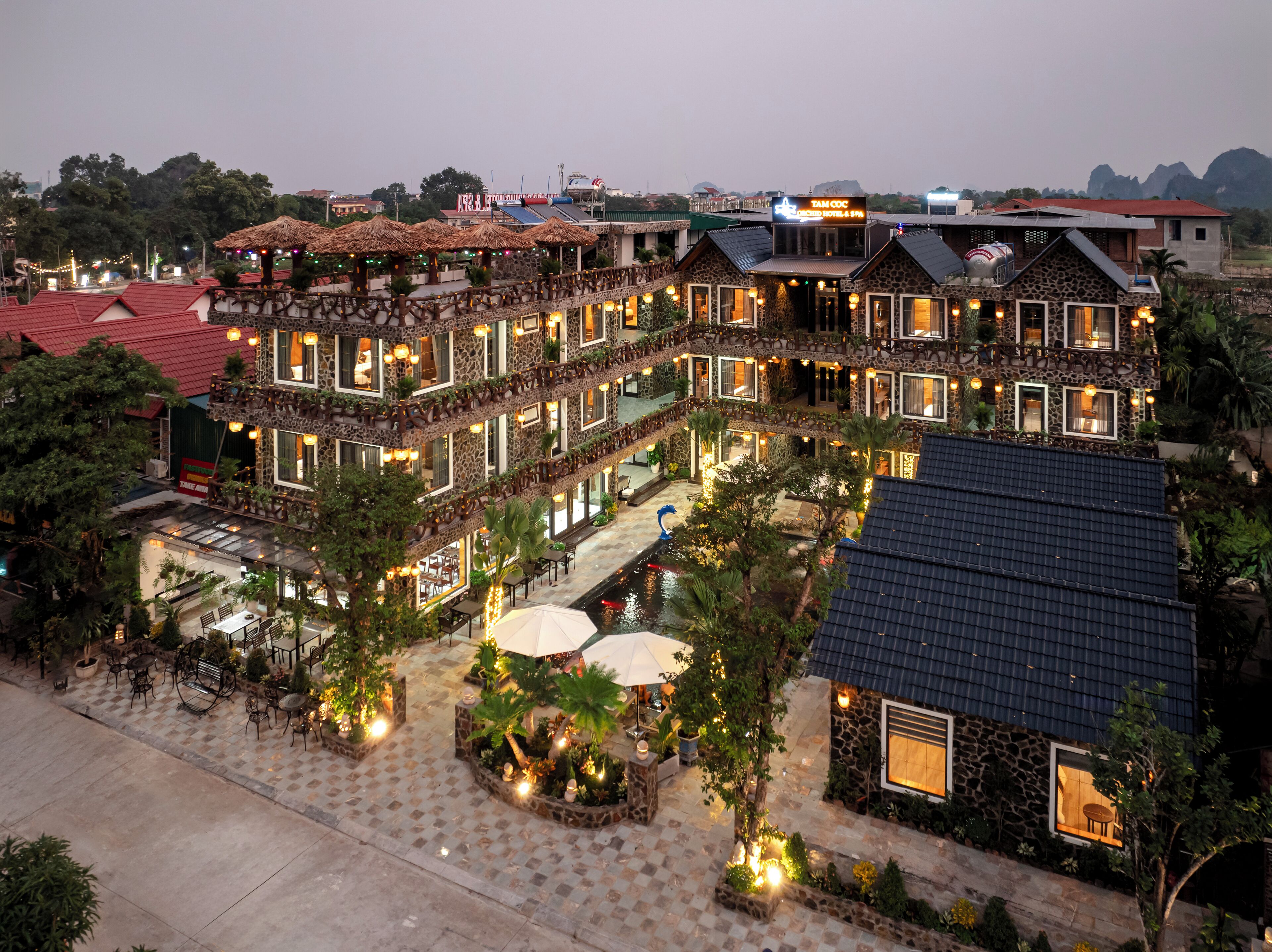 A multi-story hotel with a stone facade, outdoor seating areas, and a pool.