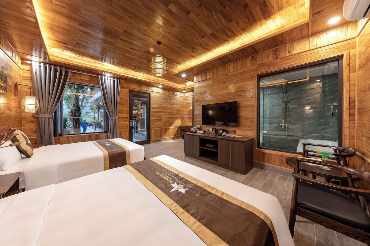 Une chambre d’hôtel avec des boiseries, deux lits, une télévision, un bureau et une grande fenêtre avec des rideaux.