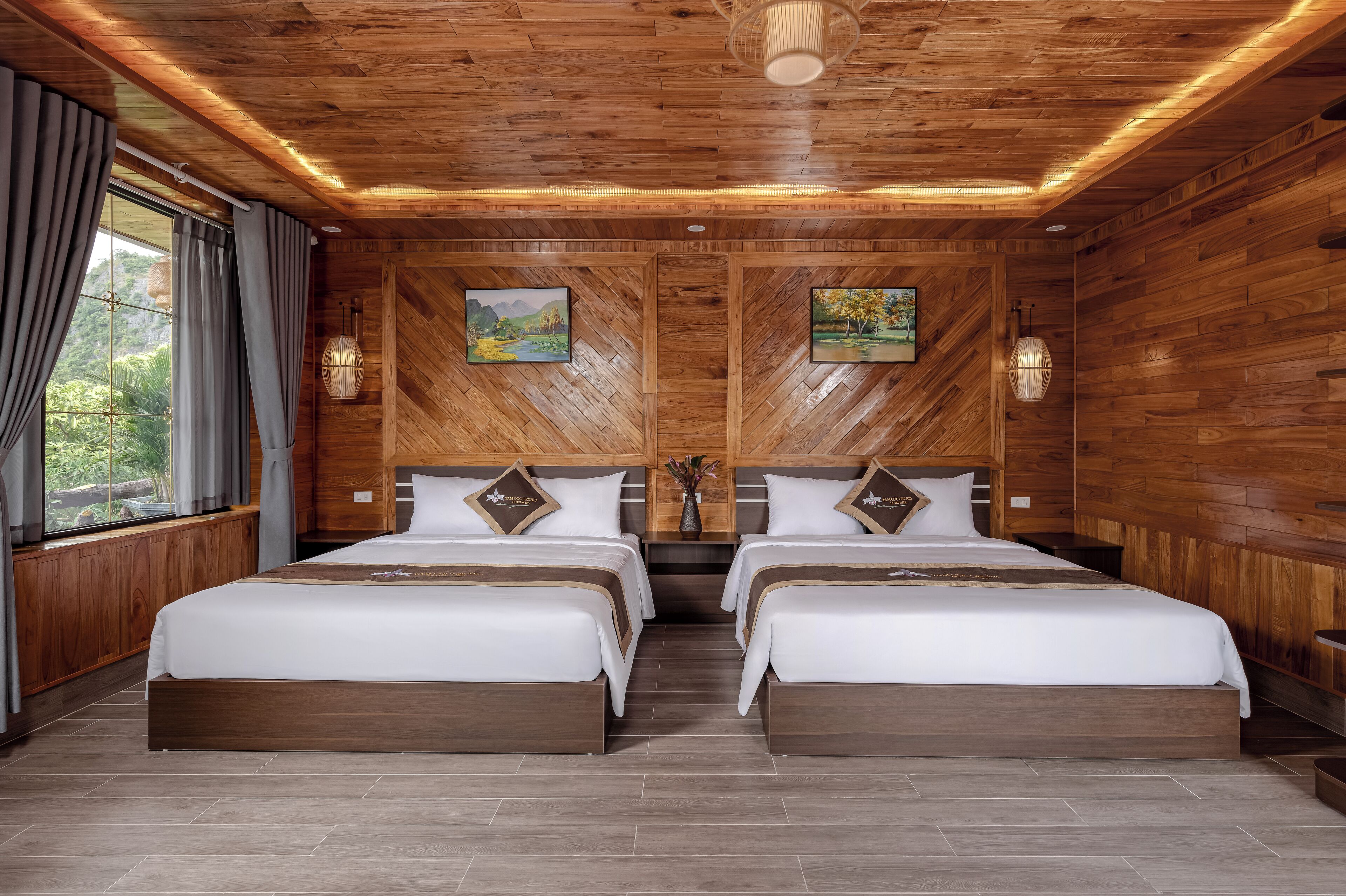 A room with two beds, wooden walls, and a large window with curtains.