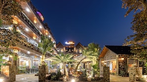 A well-lit outdoor area with stone pillars, palm trees, and a restaurant with outdoor seating. - Tam Coc Orchid Hotel & Spa (Nam Hoa Lu)