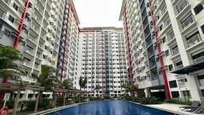 A modern residential building with a central swimming pool surrounded by palm trees and lounge chairs.