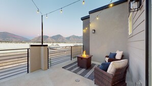 Un balcon avec un canapé en osier, une petite table avec un foyer, des guirlandes lumineuses et une vue sur les montagnes.
