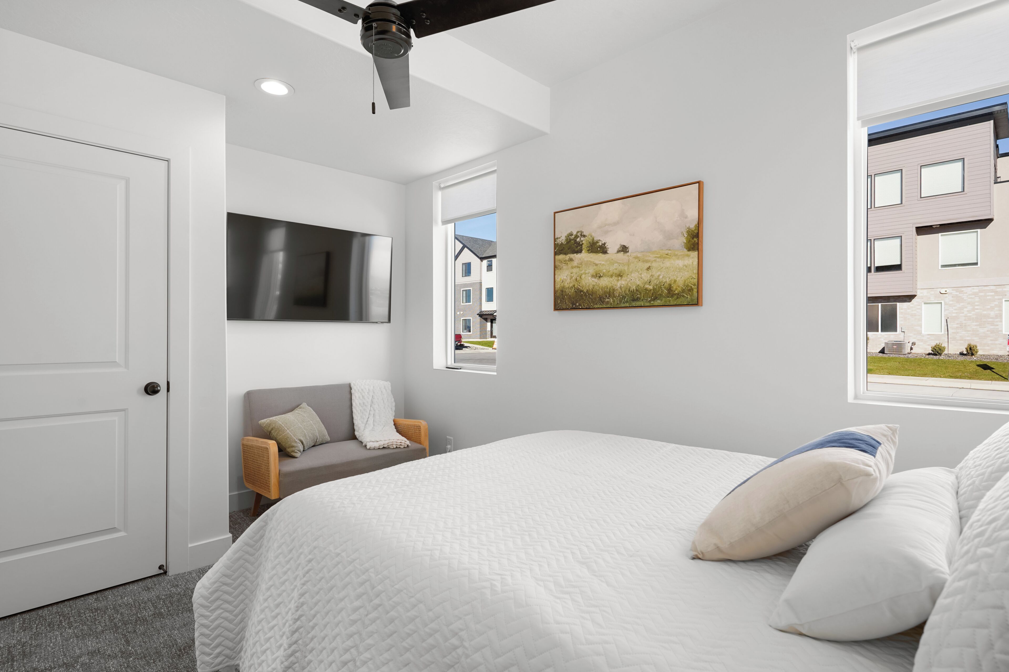 Un dormitorio moderno con una cama grande, un televisor de pantalla plana, un cuadro y una ventana con vistas a edificios.