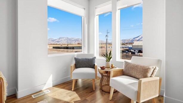 Une pièce moderne dotée de deux grandes fenêtres, d’un canapé blanc, d’un fauteuil et d’une petite table sur laquelle est posée une plante.