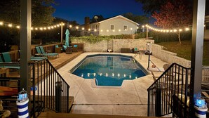 Un jardin avec une piscine, des chaises longues et des guirlandes lumineuses.