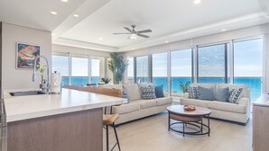Een moderne woonkamer met een groot raam met uitzicht op de oceaan, een plafondventilator en een keuken met een bar.