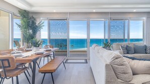 Een moderne woonkamer met een grote schuifpui naar een balkon met uitzicht op zee.