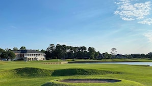 Een golfbaan met een clubhuis, een vijver en omliggende bomen.