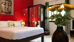 Une chambre d’hôtel avec un lit, une statue de Bouddha, un vase de fleurs et une fenêtre avec des rideaux.