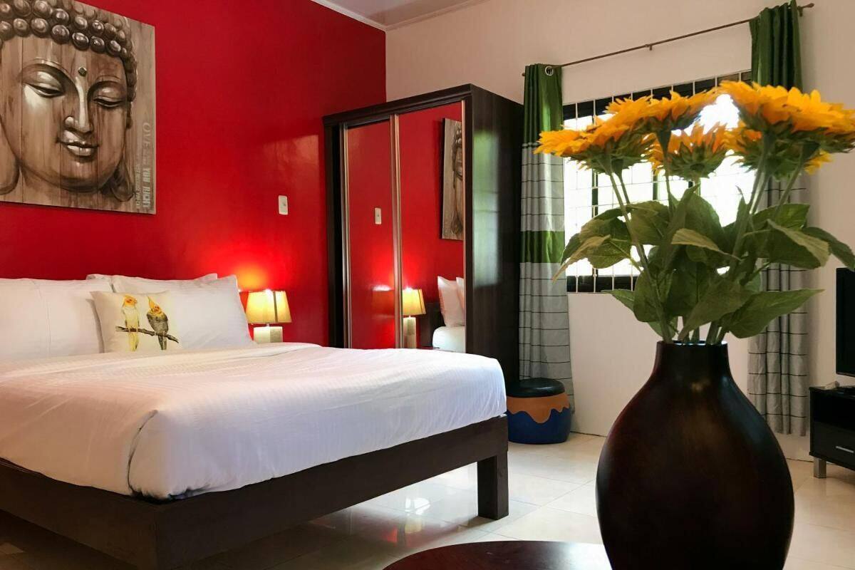Une chambre d’hôtel avec un lit, une statue de Bouddha, un vase de fleurs et une fenêtre avec des rideaux.