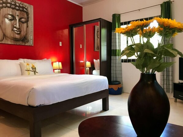 A hotel room with a bed, a Buddha statue, a vase with flowers, and a window with curtains. - Nora's Place Boutique Resort (Panglao)