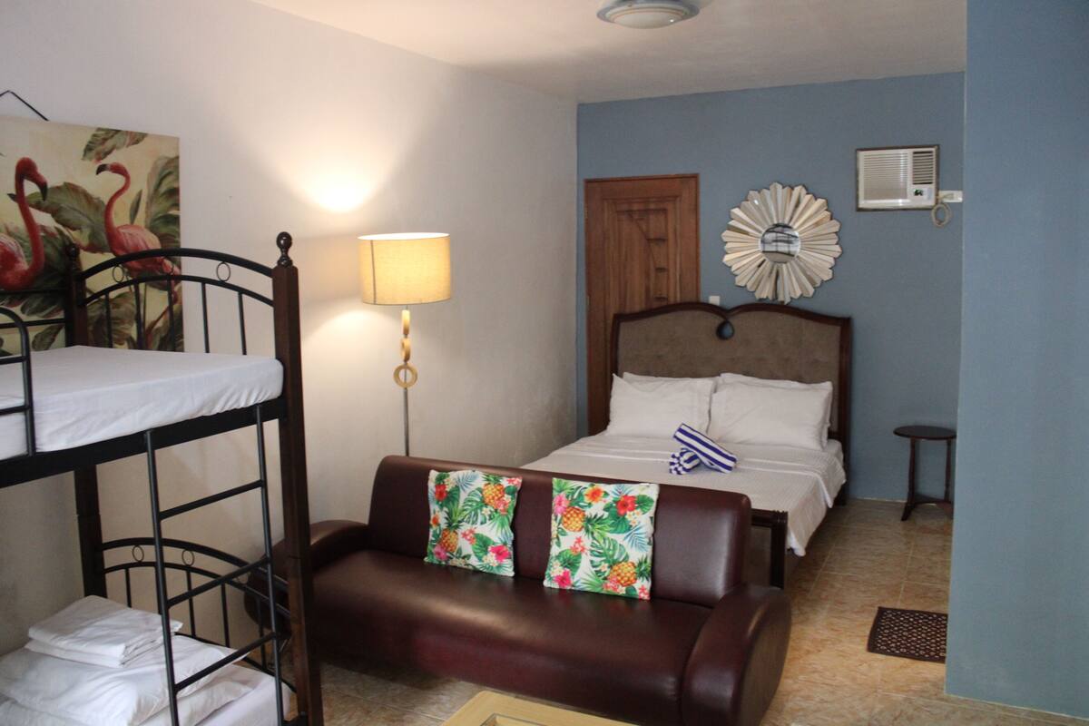Une chambre avec des lits superposés, un lit simple, un canapé en cuir marron, une lampe murale, un élément décoratif mural et une petite table.