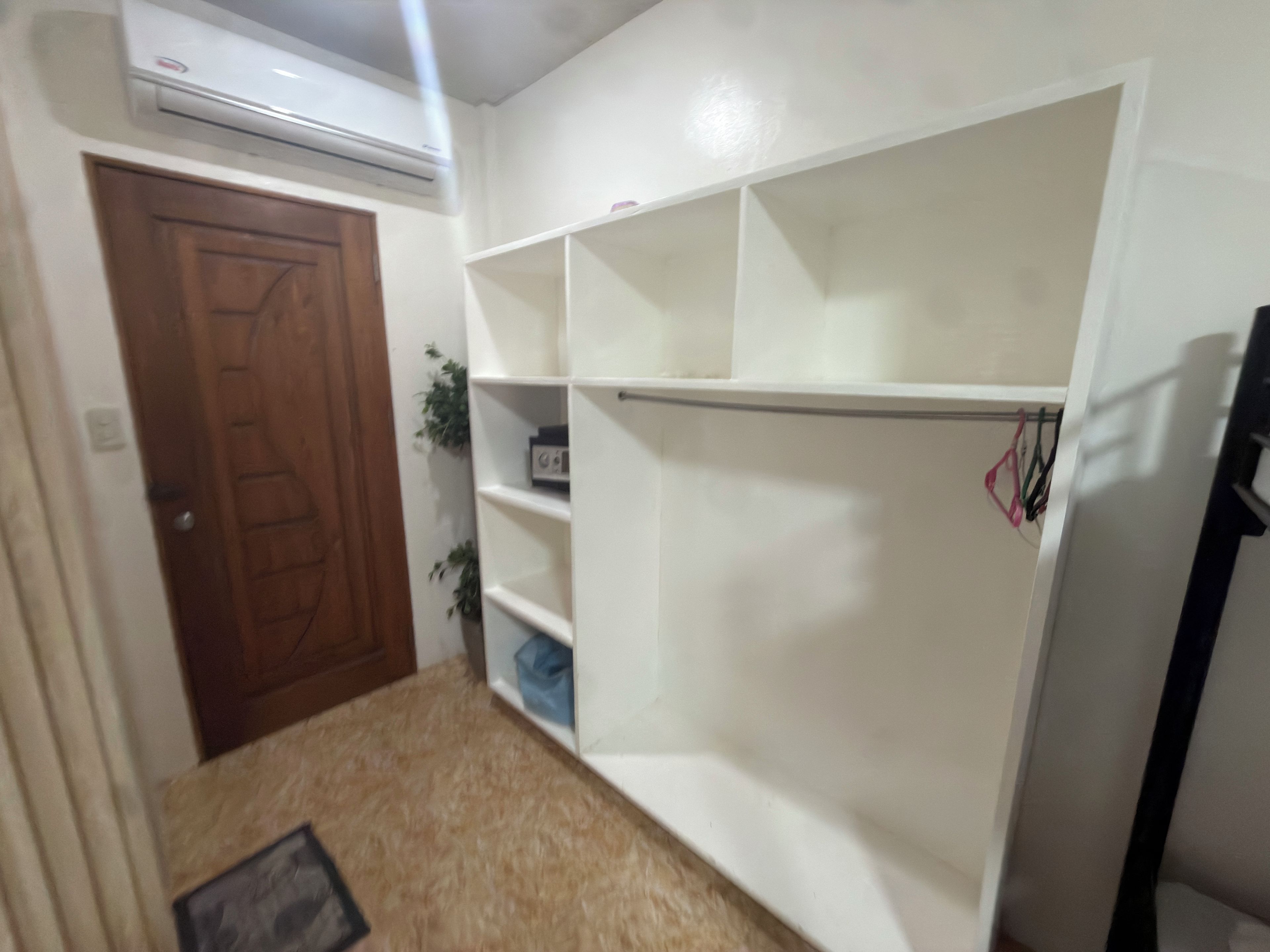 A room with a wooden door, white shelving units, and an air conditioning unit mounted on the wall.
