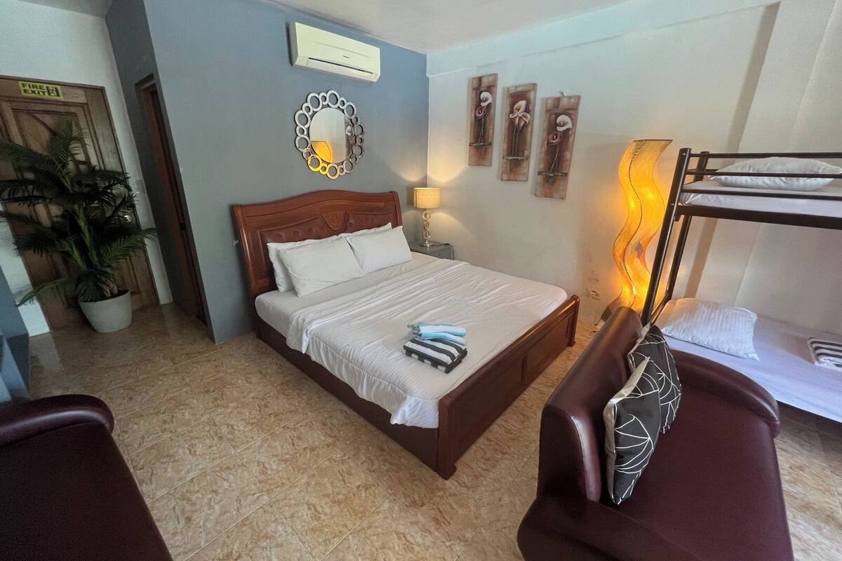 Une chambre d’hôtel avec un lit, une table de chevet, une lampe, une plante en pot, un lit superposé et une chaise.