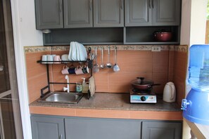 A kitchen with grey cabinets, a sink, a stove, and a kettle. - Nora's Place Boutique Resort (Panglao)