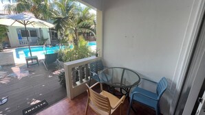 Un balcon avec une table et des chaises en verre, donnant sur une piscine et des palmiers.