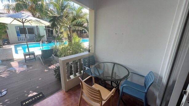 Un balcón con mesa y sillas de vidrio, con vista a una piscina y palmeras.