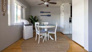Un coin repas avec une table ronde, des chaises blanches, un ventilateur de plafond et un panneau « BIENVENUE » accroché au mur.