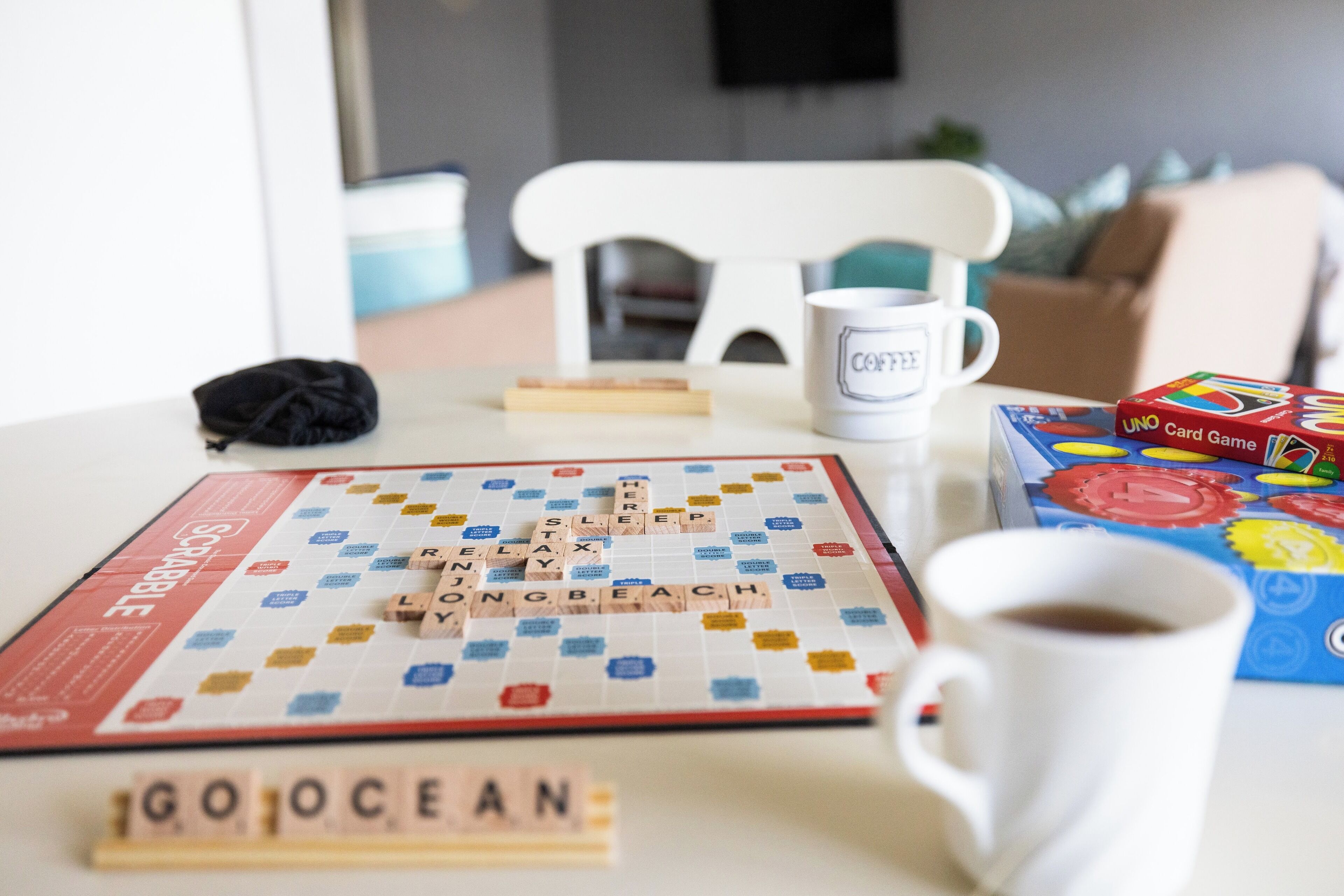 Un juego de Scrabble con fichas que deletrean 'GOOCEAN' sobre una mesa, una taza de café y una caja del juego UNO.