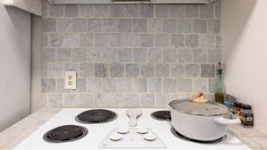 Une cuisine avec un fourneau blanc, une casserole sur le brûleur de droite et un pare-feu en carreaux gris.