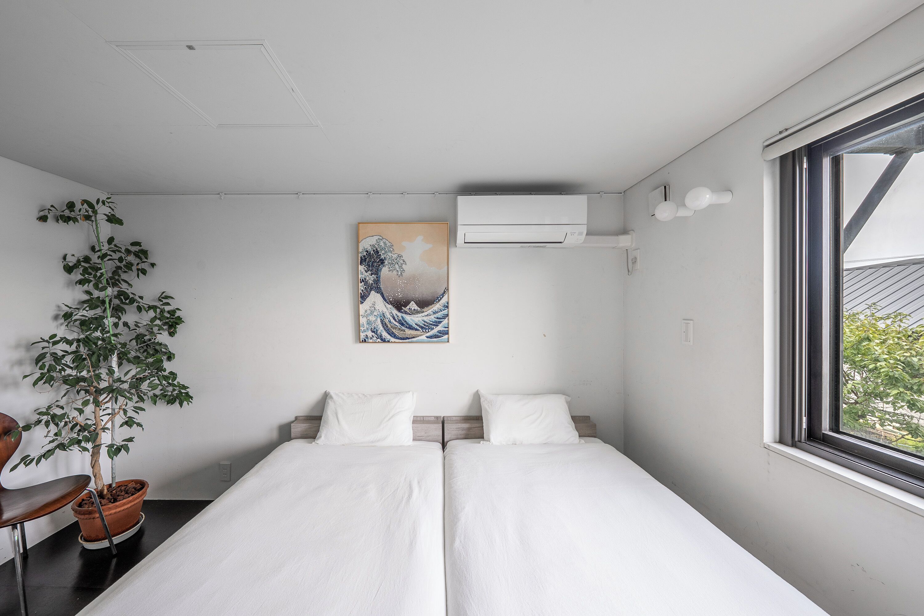 A room with two beds, a potted plant, a painting, and an air conditioning unit.