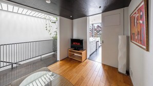 A modern living room with a wooden floor, a TV on a stand, a balcony with a railing, and a painting on the wall. - TOWNHOUSE ASAHIKAWA  (Asahikawa)
