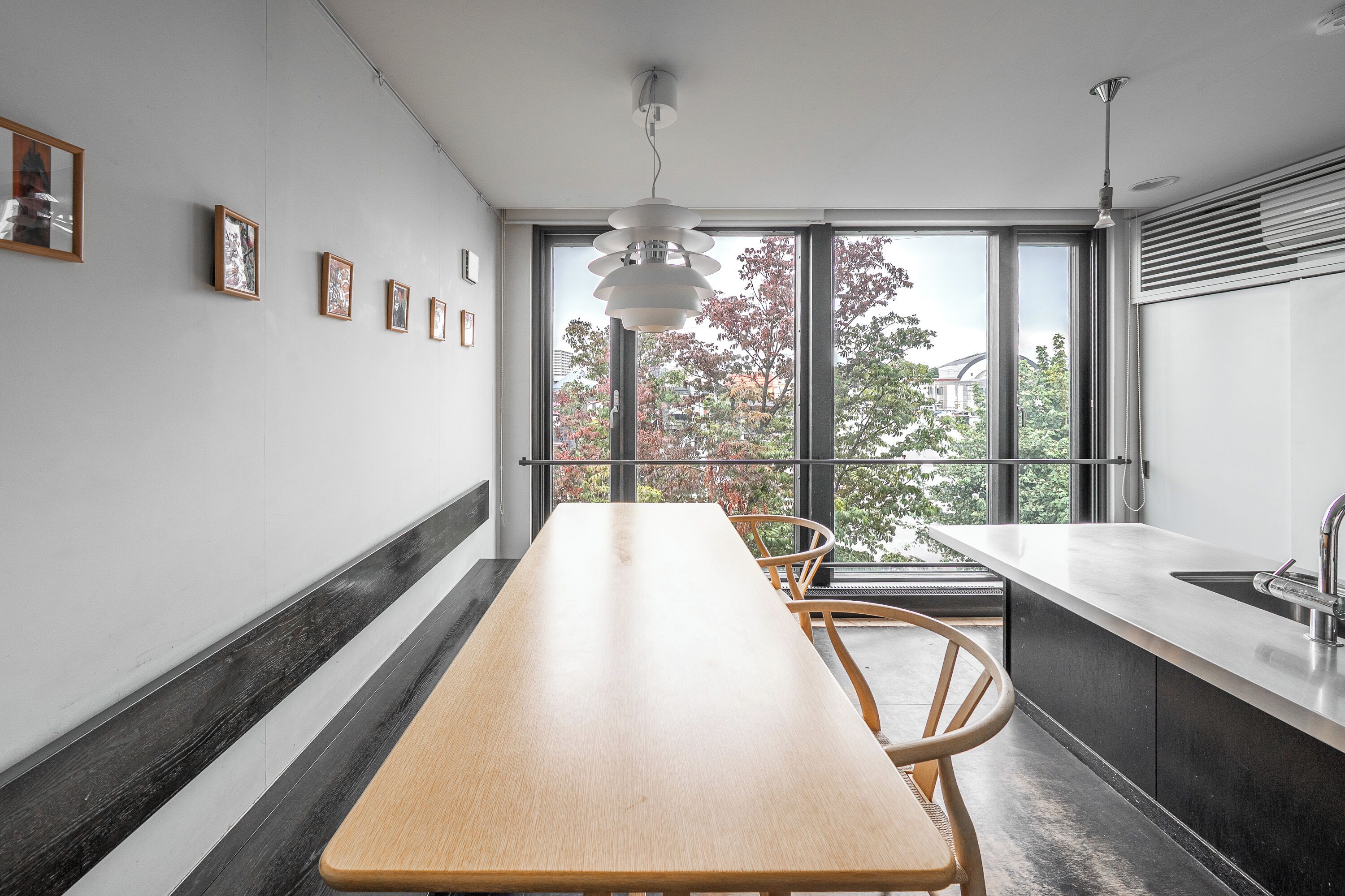 Une cuisine moderne avec une longue table en bois, un évier encastré et de grandes fenêtres donnant sur la forêt.
