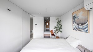 A modern hotel room with a large bed, a wooden chair, a potted plant, and a Japanese wave painting on the wall. - TOWNHOUSE ASAHIKAWA  (Asahikawa)