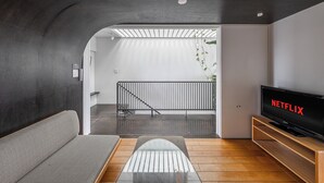A modern living room with a sofa, a glass coffee table, a wooden TV stand, and a large flat-screen TV displaying "NETFLIX". - TOWNHOUSE ASAHIKAWA  (Asahikawa)