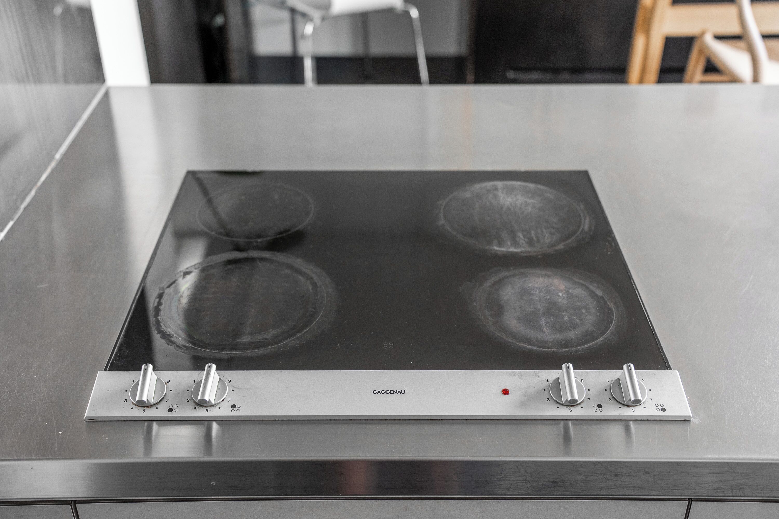 Een keuken met een roestvrijstalen kookplaat, vier branders, en een bedieningspaneel met knoppen en een rode indicatorlamp.