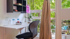 A room with a desk, chair, window with curtains, and a view of greenery outside.