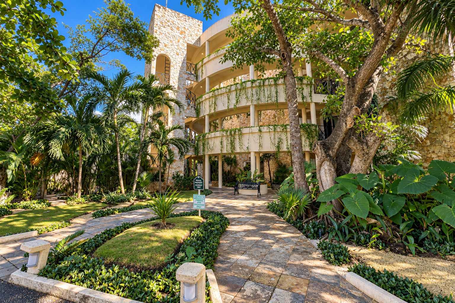 Un patio con un edificio de piedra, palmeras y un camino pavimentado.