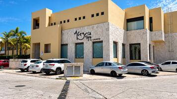 A hotel with a stone facade, multiple parking spaces, and palm trees in the background.