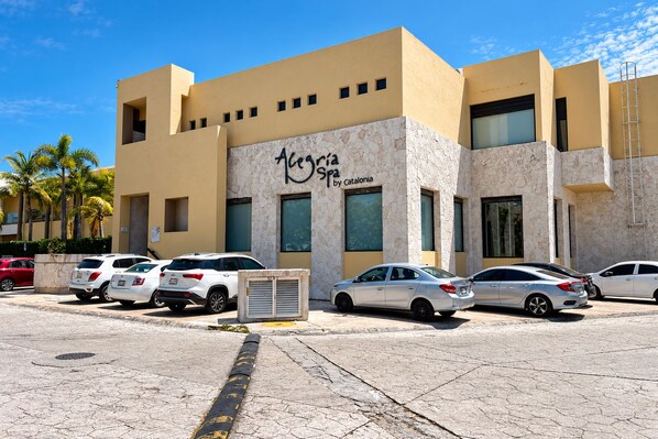 A hotel with a stone facade, multiple parking spaces, and palm trees in the background. - High-End Waterfront Condo Secrets Waters (Puerto Aventuras)