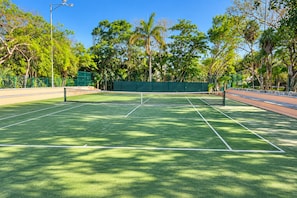 A tennis court with a net, surrounded by trees and a fence. - High-End Waterfront Condo Secrets Waters (Puerto Aventuras)