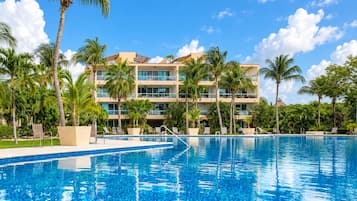A hotel with a swimming pool, palm trees, and a clear blue sky.