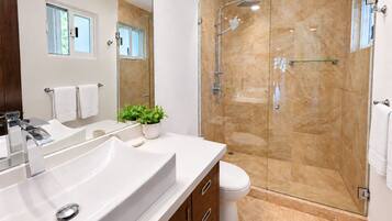Un baño moderno con un lavamanos grande de color blanco, un box de ducha con paredes de vidrio y un inodoro.