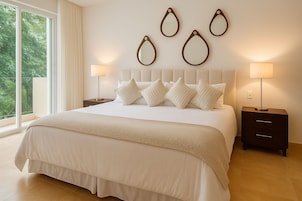 Un dormitorio moderno con una cama grande, varios almohadones, una mesita de noche con lámpara y espejos en la pared.