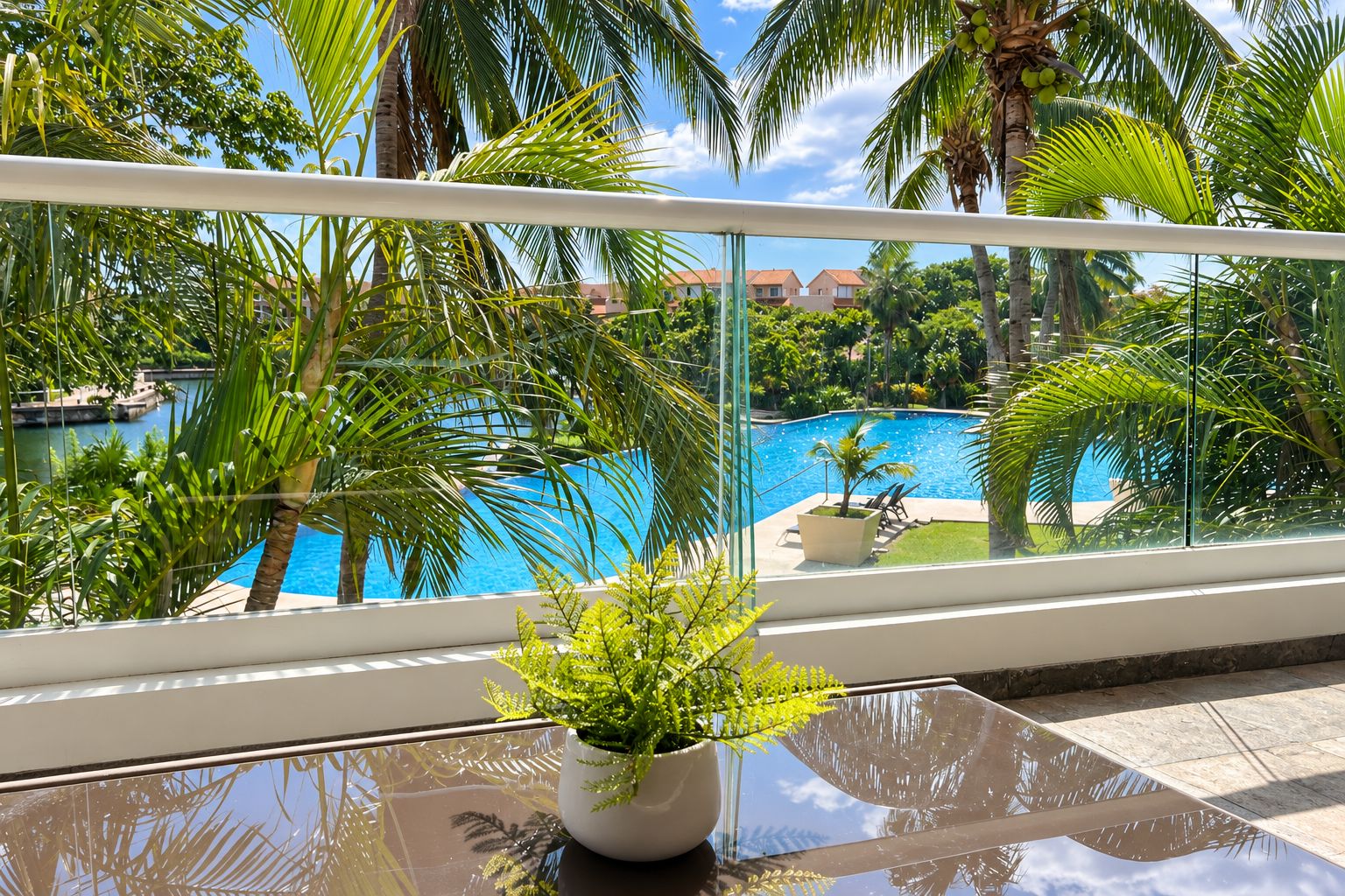 Un balcón con vista a una piscina rodeada de palmeras y un cielo despejado.