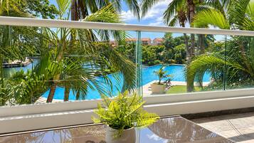 Un balcón con vista a una piscina rodeada de palmeras y un cielo despejado.
