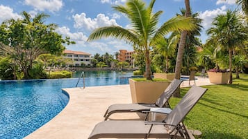 Un área junto a la piscina con sillones de descanso, palmeras y cielo despejado.