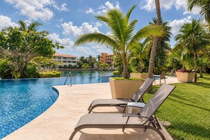 Un área junto a la piscina con sillones de descanso, palmeras y cielo despejado.