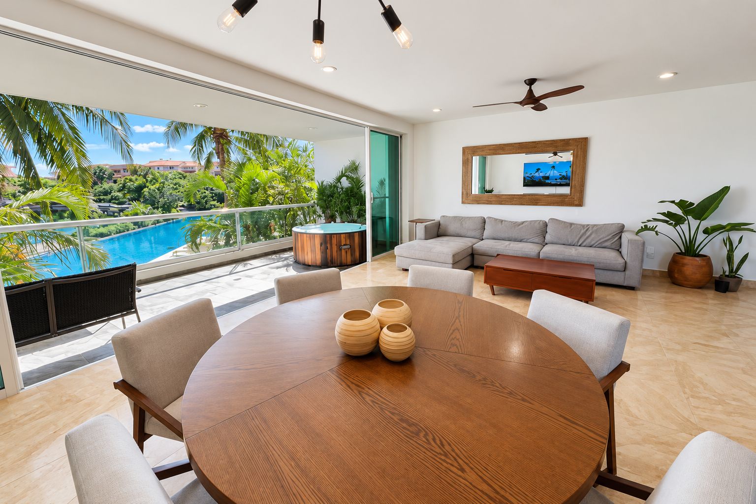 A modern living room with a round wooden table, grey sofa, and a ceiling fan.