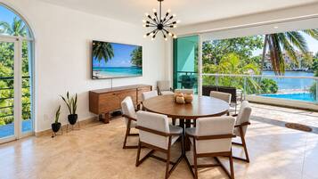 A spacious dining area with a round table, chairs, and a view of a pool and palm trees.