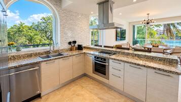 Cocina moderna con una isla grande, electrodomésticos de acero inoxidable y vistas a una piscina y vegetación.