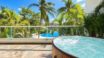 Un jacuzzi en un balcón con vista a una piscina y palmeras.