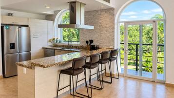 A modern kitchen with a central island, stainless steel appliances, and a large window overlooking greenery.