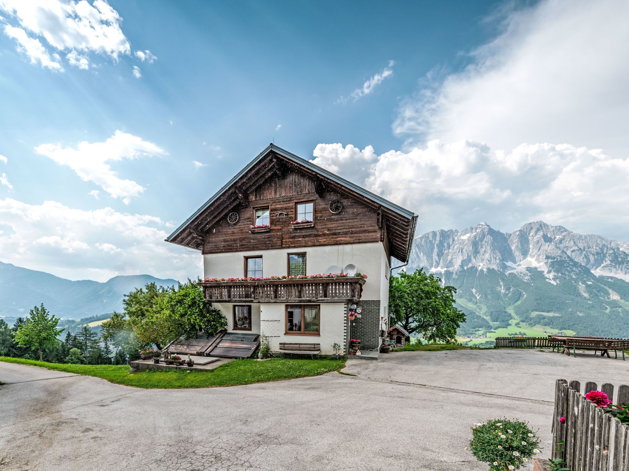 Ein zweistöckiges Holzhaus mit Balkon, umgeben von Bergen und einem klaren Himmel.